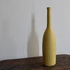 a yellow ceramic bottle on a wooden table it's by ceramicist Lucy Burley.