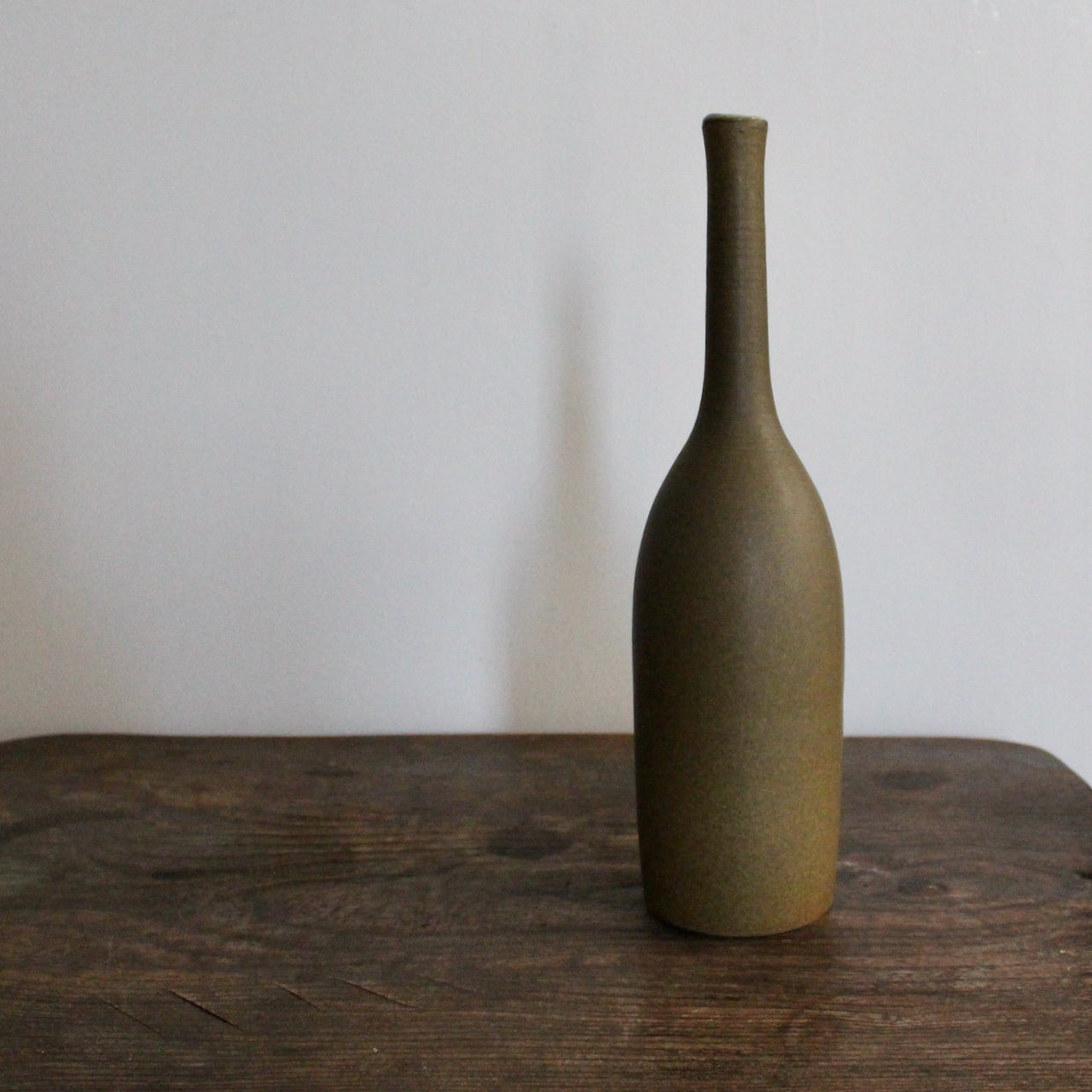 olive coloured ceramic bottle on a wooden table it's by UK ceramicist Lucy Burley 