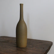 an olive coloured ceramic bottle on a wooden table it's by UK ceramic artist Lucy Burley 
