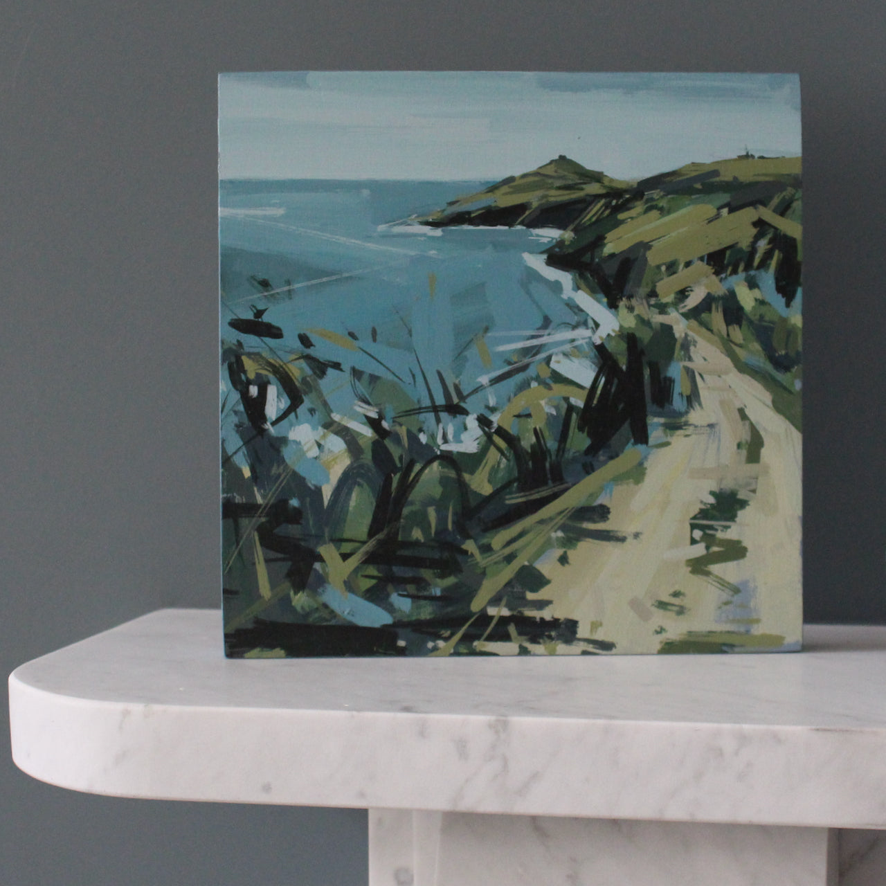 Imogen Bone landscape painting of Rame Head in south east Cornwall showing headland in greens and browns and sea in blue sitting on top of a marble fireplace 