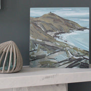 Painting of Rame Head in south east Cornwall in autumn colours with a pale blue sea and sky painted by Imogen Bone  - the painting is standing on a marble mantle piece next to small ceramic sculpture 