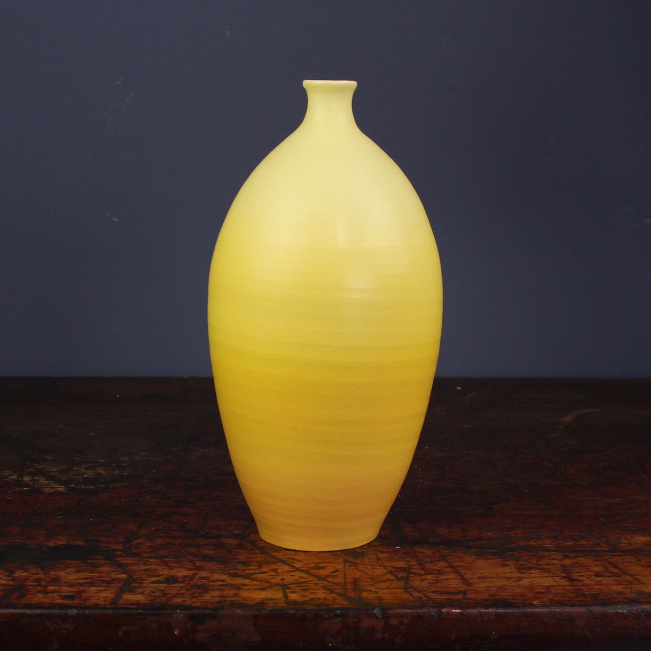 A Tall yellow curved bottle by Lucy Burley on a wooden table