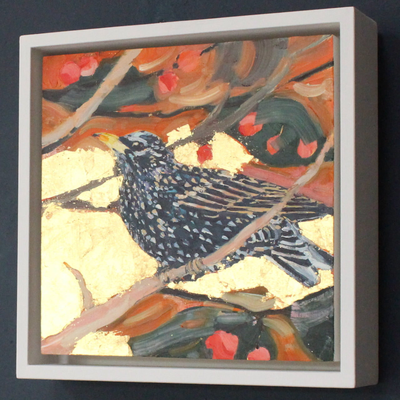 a framed Jill Hudson painting of a starling on a branch with and orange and gold background