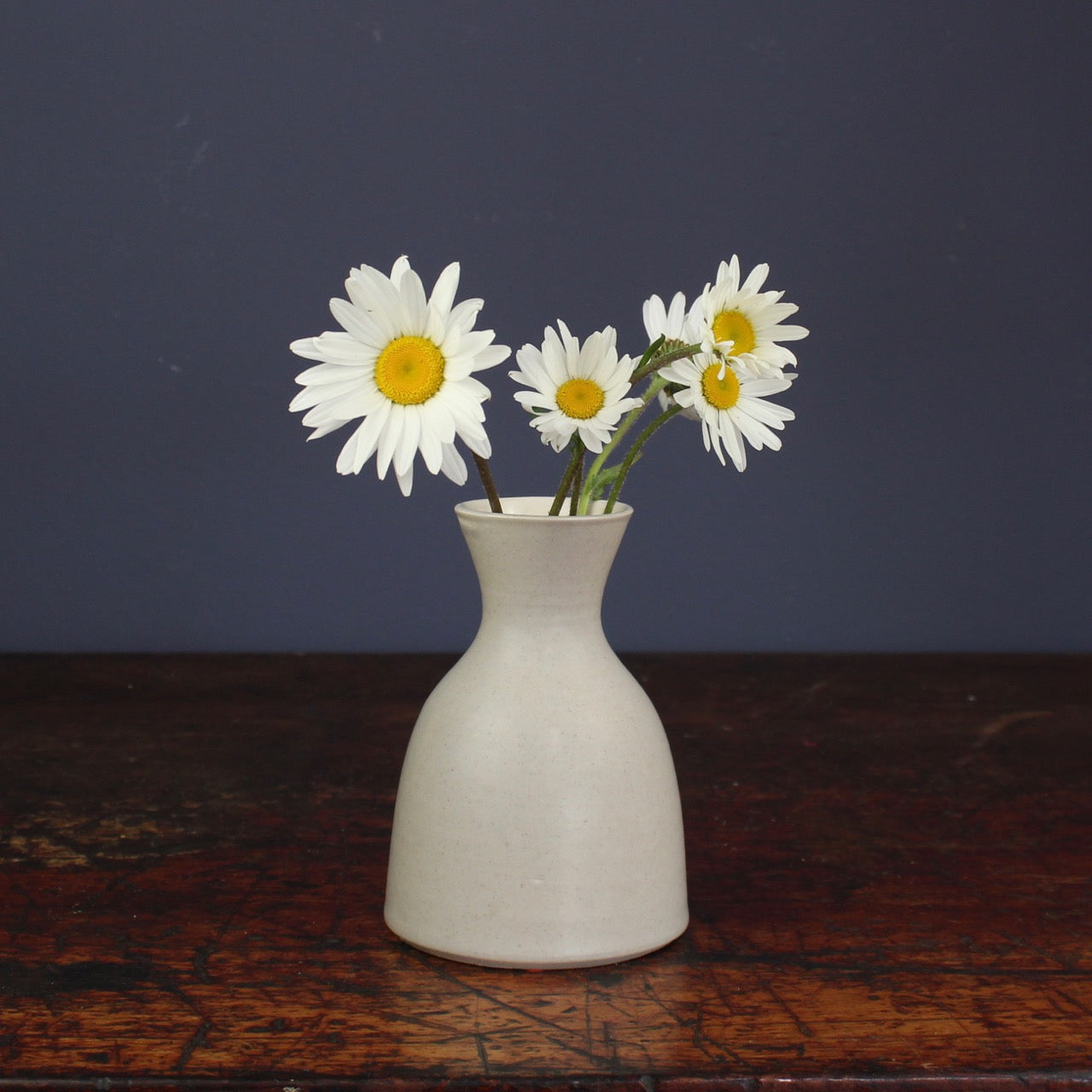 small grey curved ceramic made by Lucy Burley  with white and yellow daisies in it.