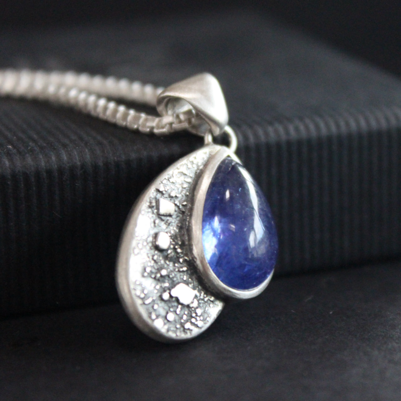 a Carin Lindberg pendant of a teardrop textured silver and blue stone on a silver chain.
