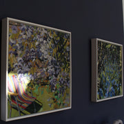 Two paintings on a dark wall one with a deckchair under a purple flowering tree, the other of bluebells in a wood