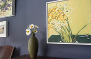 Dark green bottle with daisies in it next to painting of daffodils 