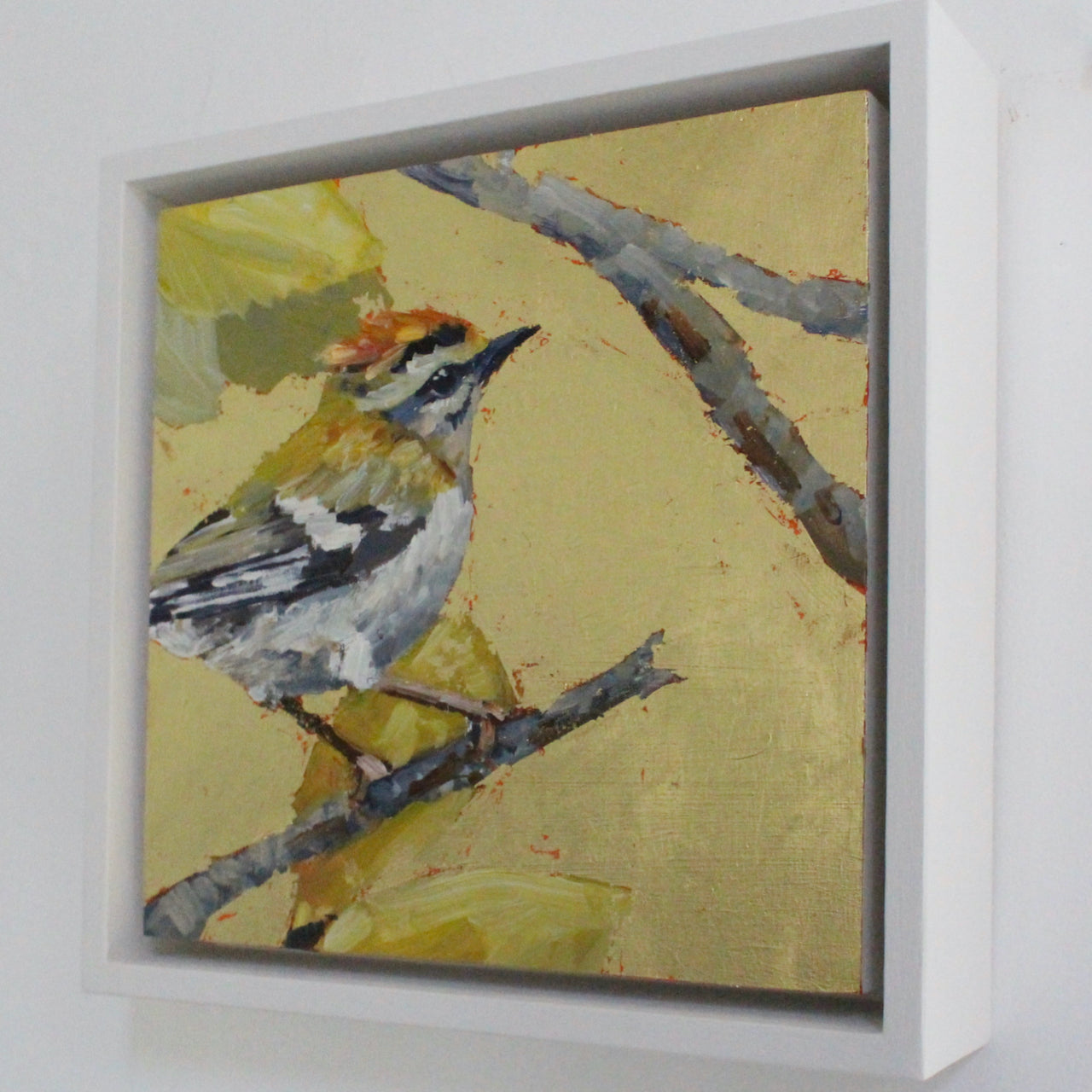 a framed Jill Hudson painting of Fire Crest bird on a twig with a gold leaf background 