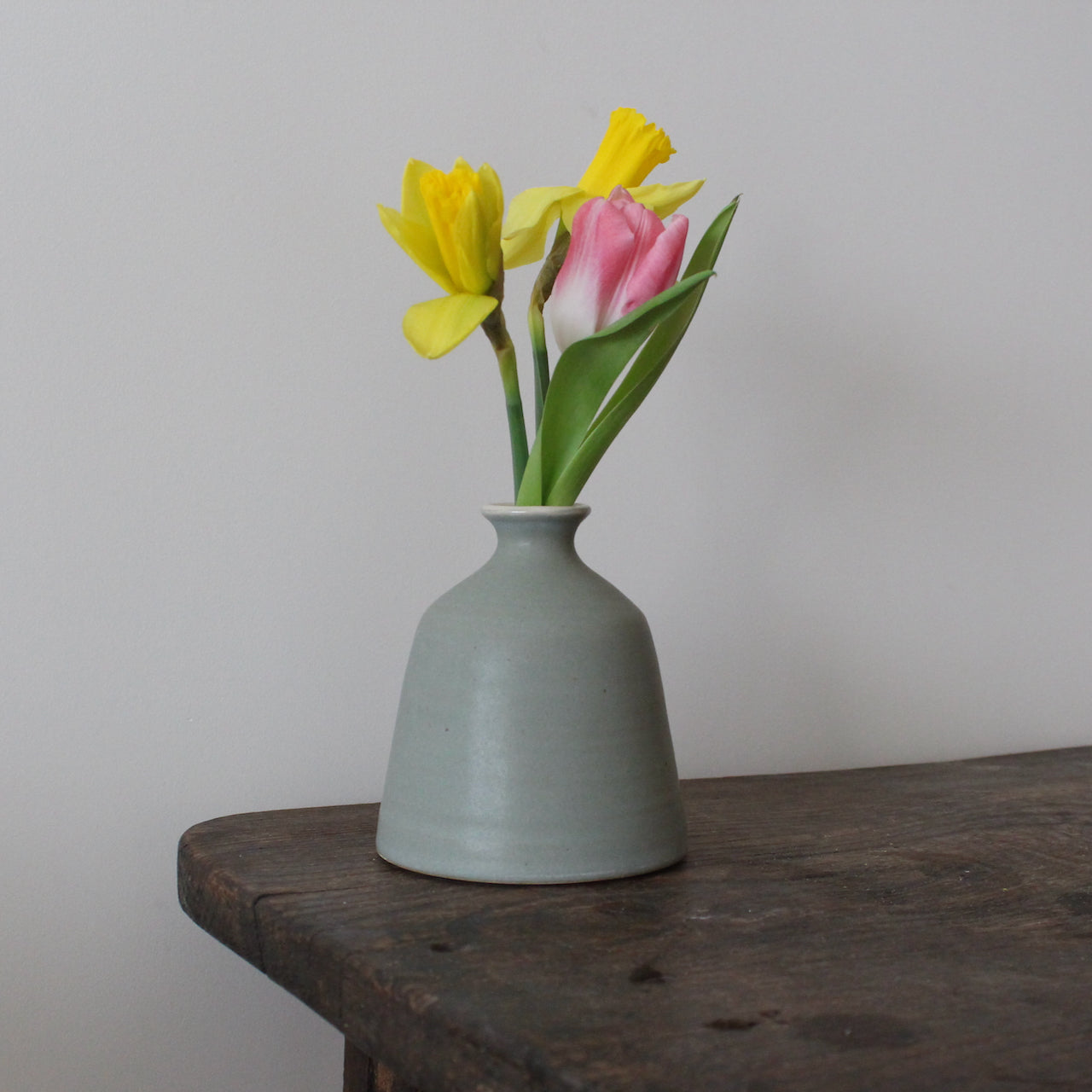 EOT ceramics bud vase in greeny grey glaze with two daffodils and a pink tulip in it