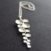 A Long sliver pendant of small circles attached to central curved line made by Beverly Bartlett 