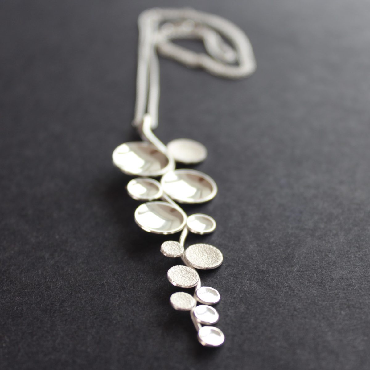 Long sliver pendant of small circles attached to central curved line made by Beverly Bartlett