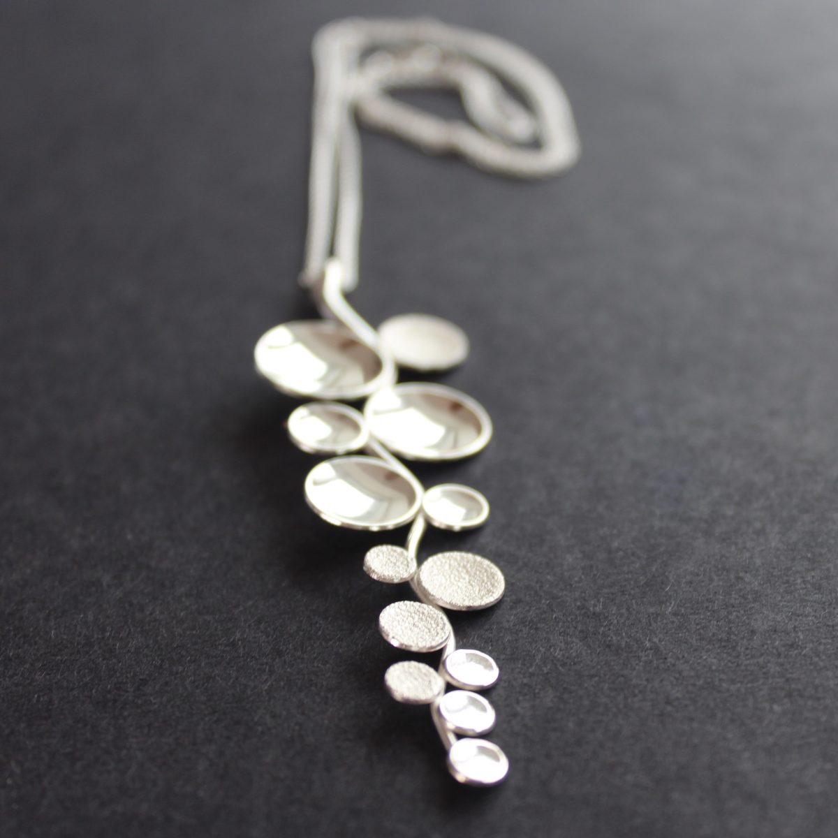 Long sliver pendant of small circles attached to central curved line made by Beverly Bartlett 