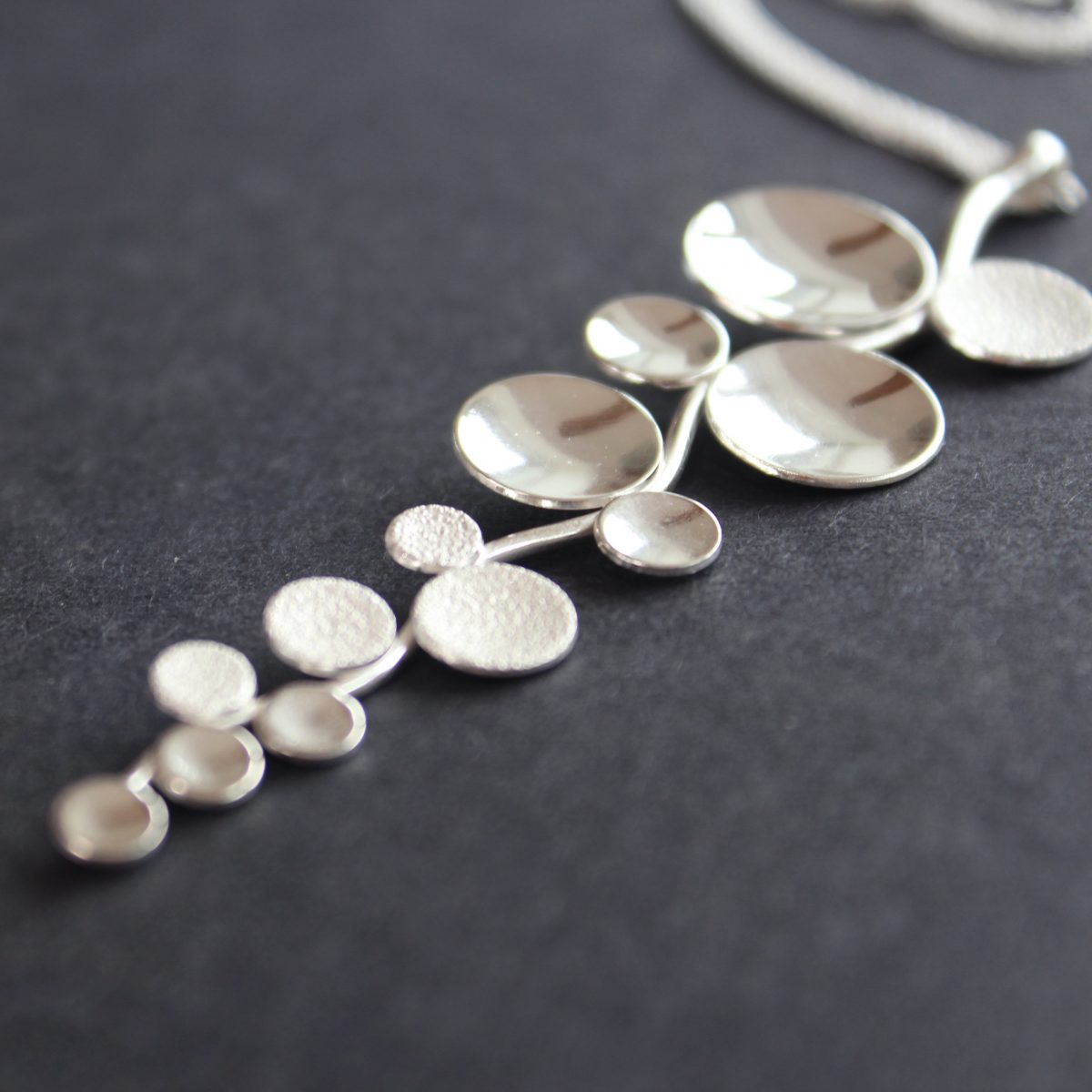 Long sliver pendant of small circles attached to central curved line made by Beverly Bartlett 