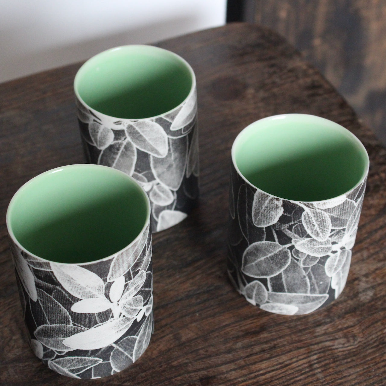 UK ceramicist Heidi Harrington trio of small ceramic beakers with a black and white photo image of leaves on the the exterior and green interior.