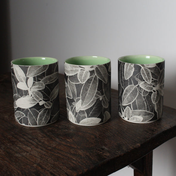a trio of small ceramic beakers by  UK ceramicist Heidi Harrington with a black and white photo image of leaves on the the exterior and green glazed interior.