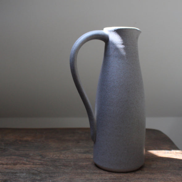 a soft grey coloured ceramic jug with handle by Lucy Burley on a wooden table in the sunlight 