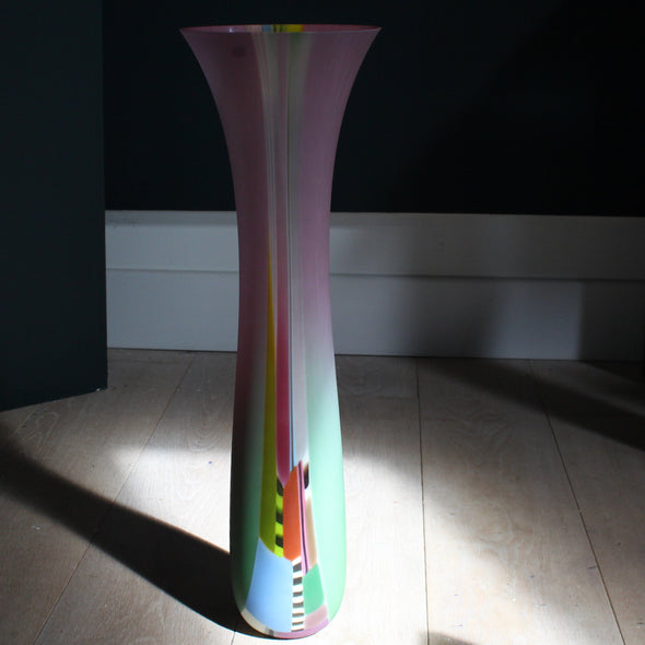 an extra tall Ruth Shelley glass vase in shades of pink with central stripe d section in blues , red and greens 