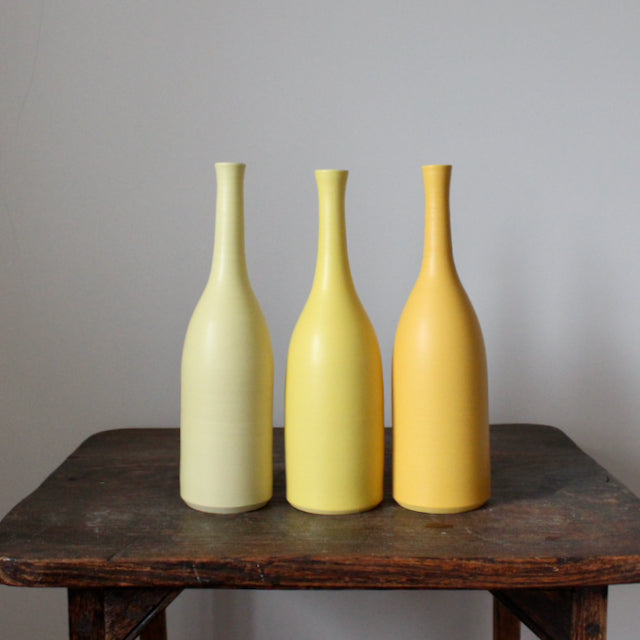 A trio of Lucy Burley ceramic bottles in shades of yellow on a wooden table.