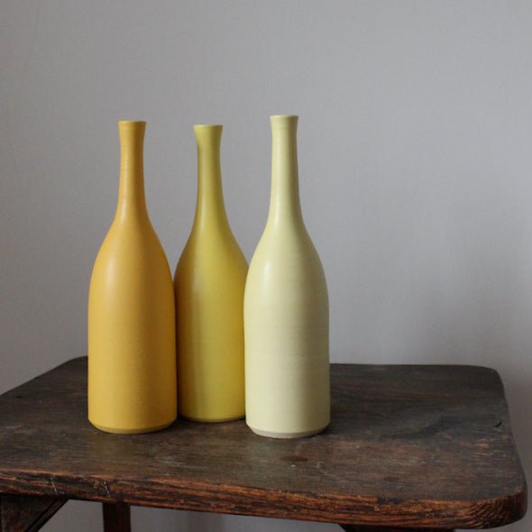 A trio of Lucy Burley ceramic bottles in shades of yellow  sitting on a wooden table.