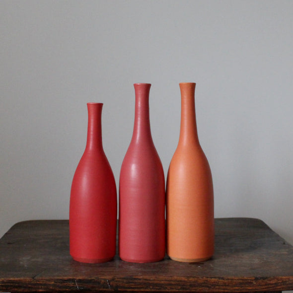 Trio of  Lucy Burley ceramic bottles in shades of red and orange  on a wooden table.