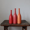 three Lucy Burley ceramic bottles in shades of red and orange sitting on a wooden table