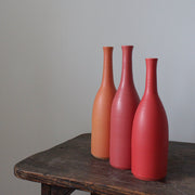 three Lucy Burley ceramic bottles in shades of red and orange.