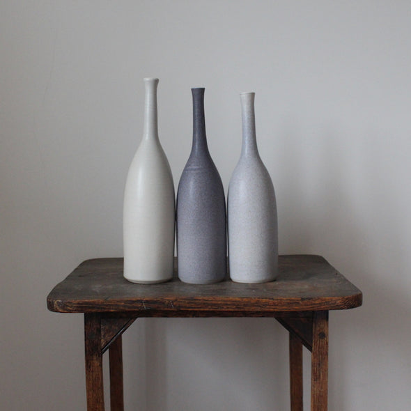 Trio of ceramic bottles in shades of grey on a wooden table by Lucy Burley 