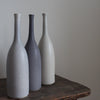 Trio of ceramic bottles in shades of grey on a wooden table  by potter Lucy Burley. 