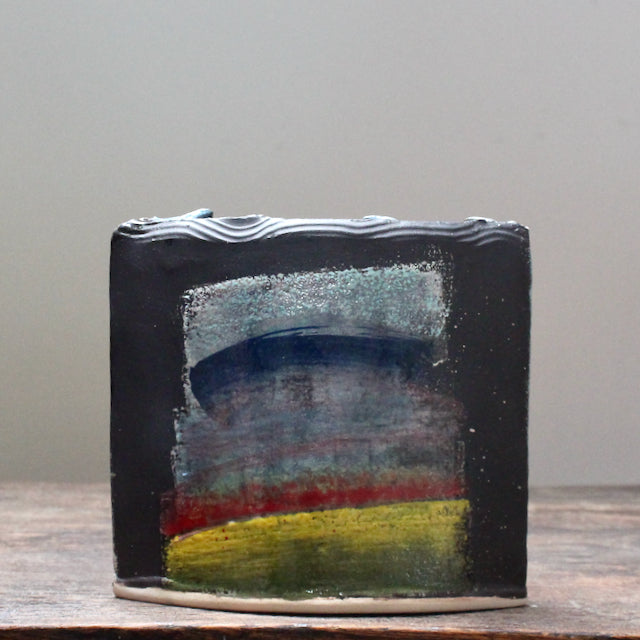 A dark ceramic vessel with rainbow style glaze by potter John Pollex.