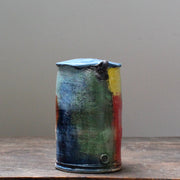 the side view of a ceramic vase with a tapered top and small lug handles by John Pollex, British potter, it is multi coloured with a blue top.