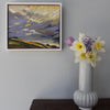 An abstract landscape painting in purples, greens and yellows on a wall next to a tall vase holding purple and yellow flowers
