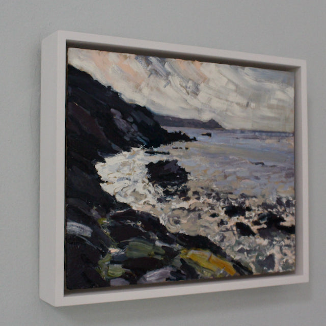 A framed painting of Rame Head in Cornwall by Jill Hudson, called From the Rocks  showing grey sea with dark cliffs