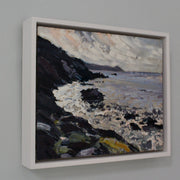 A framed painting of Rame Head in Cornwall by Jill Hudson, called From the Rocks  showing grey sea with dark cliffs 