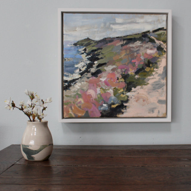 small vase with white blossom in it on a wooden table next to a painting of Rame Head in Cornwall by Jill Hudson