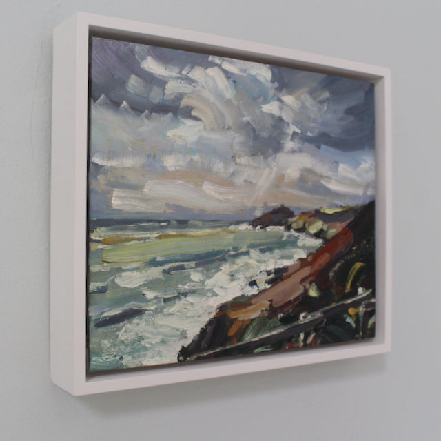 Framed painting showing cloudy skies and the coastline by Cornwall artist Jill Hudson