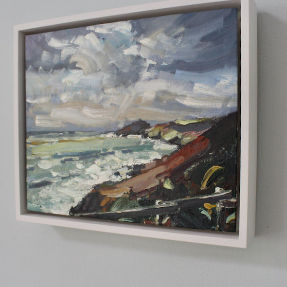 A Framed painting showing cloudy skies and the coastline by Cornwall artist Jill Hudson called Winter Walk 