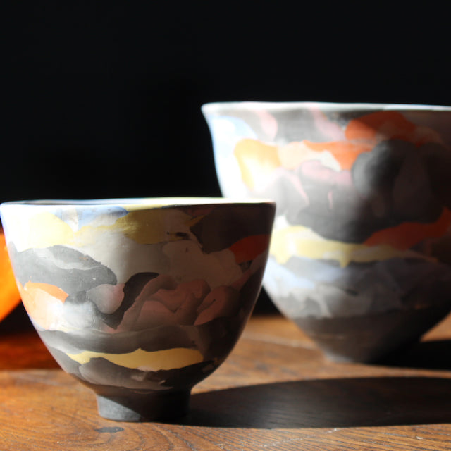 two porcelain Nerikomi style bowls in dark purple, orange and yellow by ceramic artist Judy Mckenzie. 