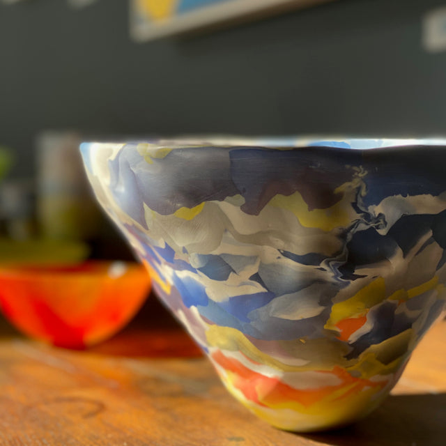 large porcelain Nerikomi bowl in orange, blue and white  by Judy McKenzie taken in the sunshine next to an orange glass bowl.