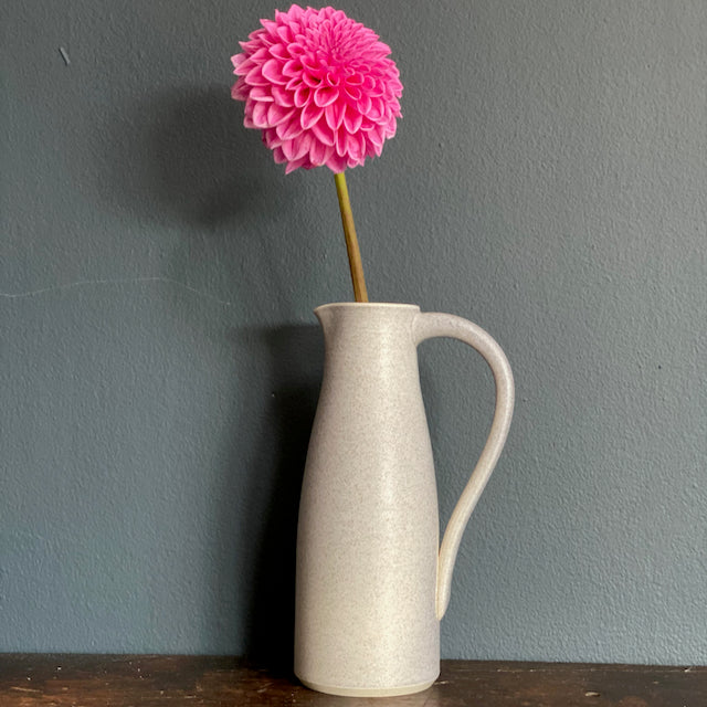 a soft grey coloured ceramic jug with handle by Lucy Burley  with  pink flower in it