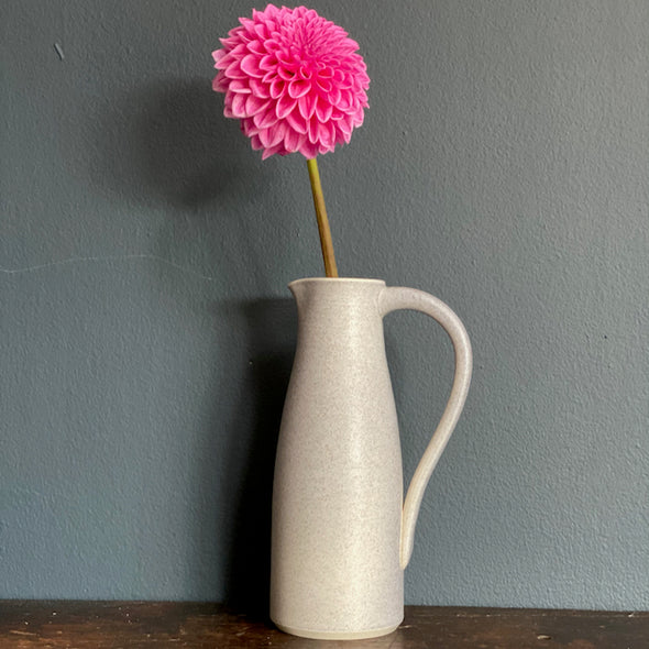 a soft grey coloured ceramic jug with handle by Lucy Burley  with  pink flower in it 