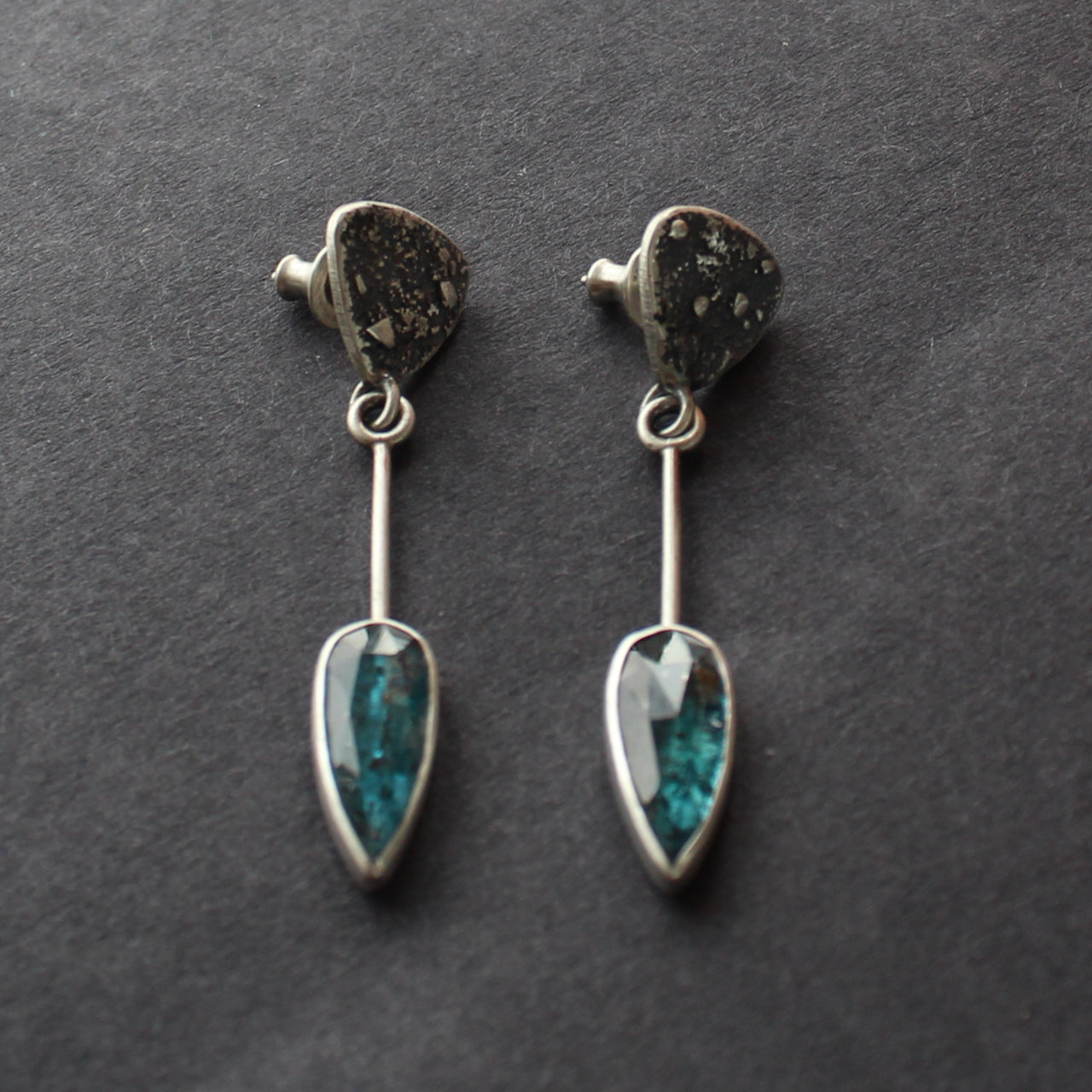 Long sliver earrings with a textured silver triangle falling to green oval shaped stones set in plain silver