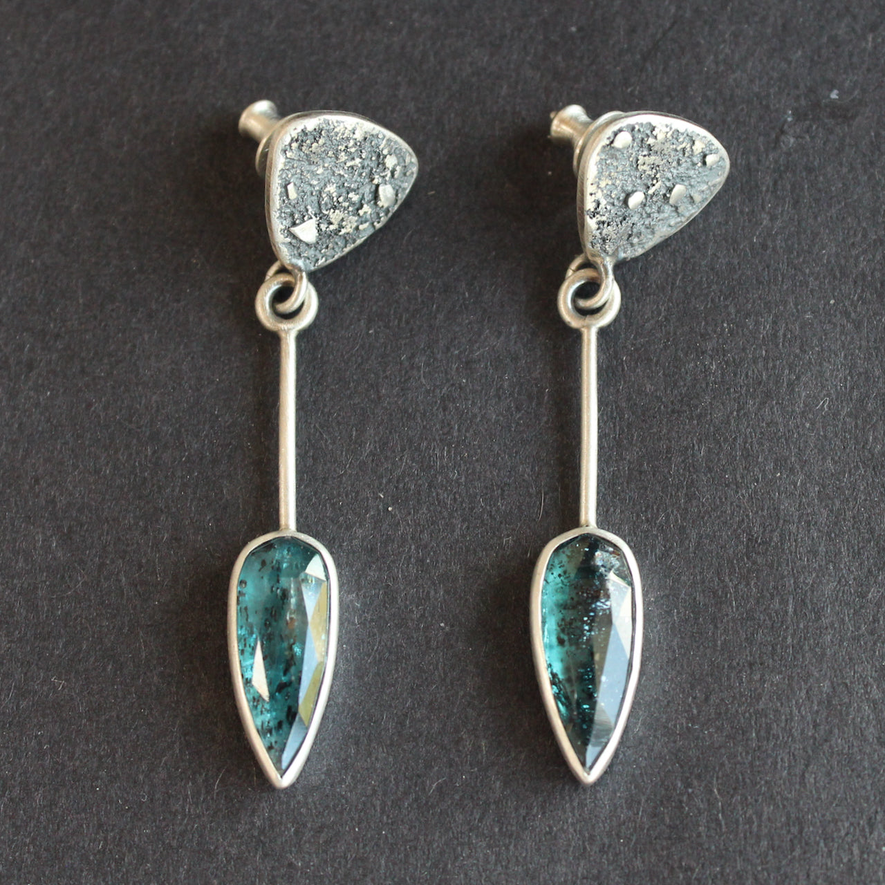 Long sliver earrings with a textured silver triangle falling to green oval shaped stones set in plain silver