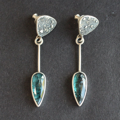 Long sliver earrings with a textured silver triangle falling to green oval shaped stones set in plain silver 