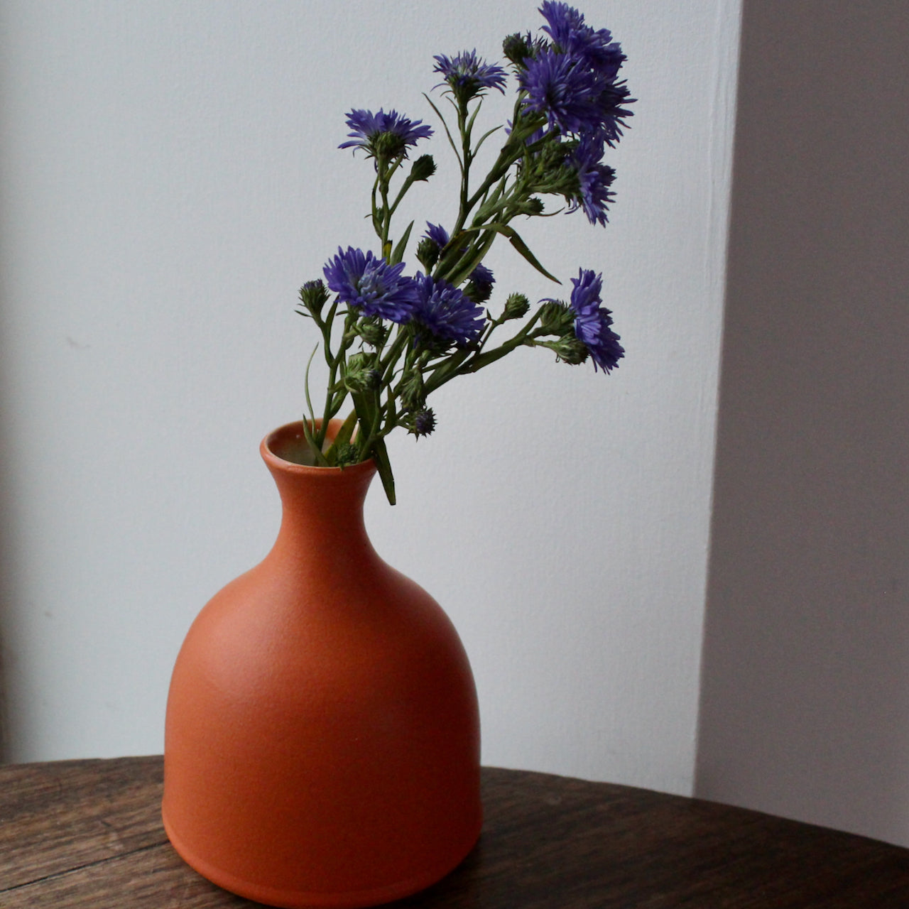 a  Lucy Burley small orange coloured ceramic bud vase with purple flowers in it