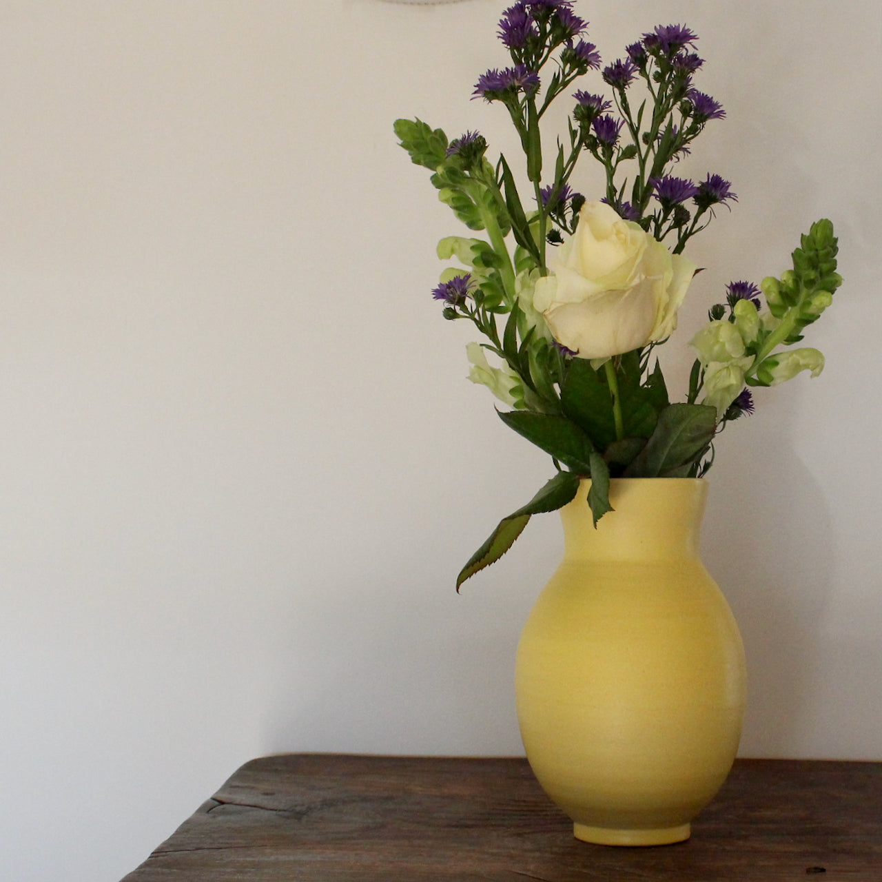 yellow vase by UK ceramic artist Lucy Burley  with green, white and purple flowers in it