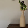 cream coloured ceramic vase by UK ceramic artist Lucy Burley with purple and green flowers in it