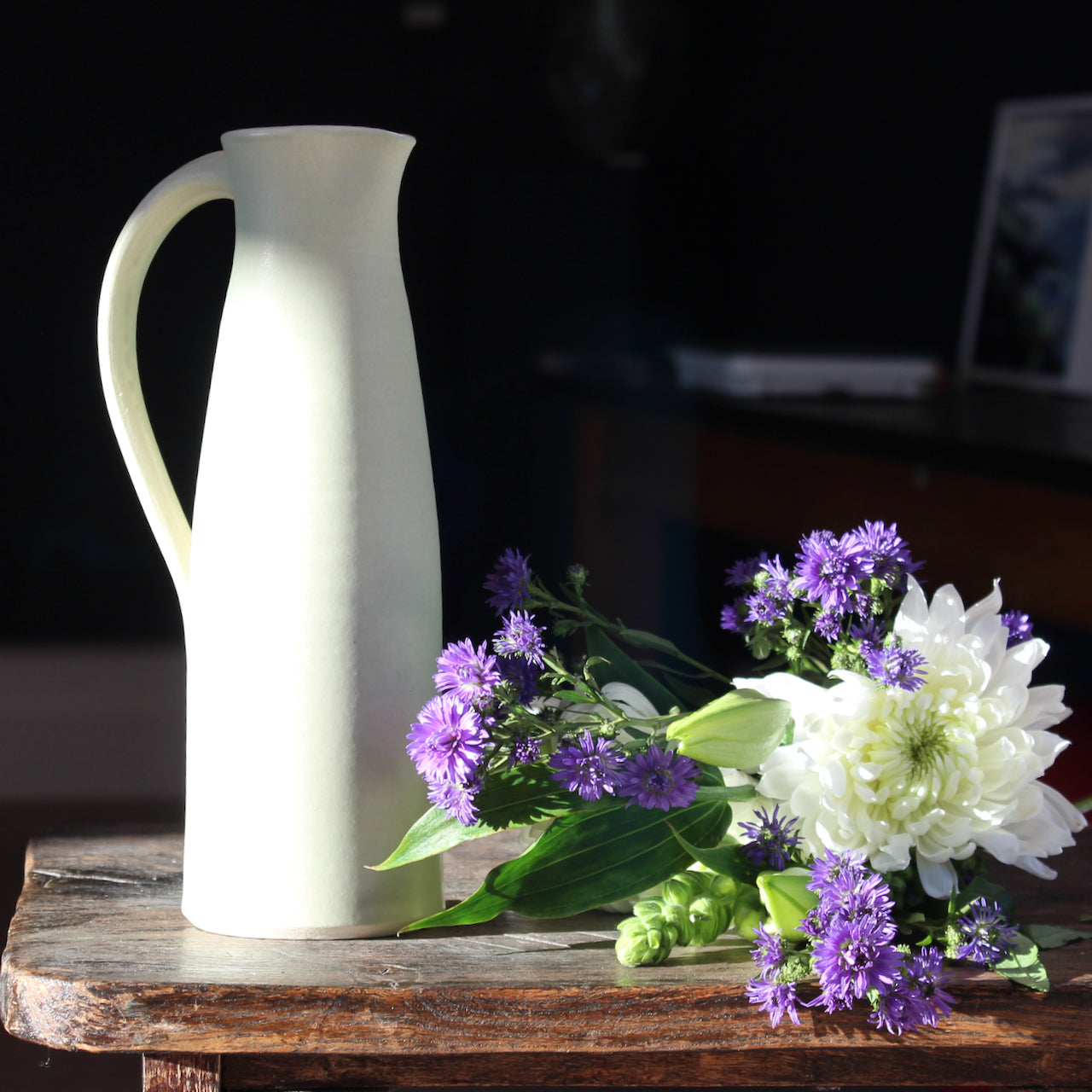 pale olive ceramic jug by UK ceramicist Lucy Burley with a bunch of white and purple flowers lying beside it