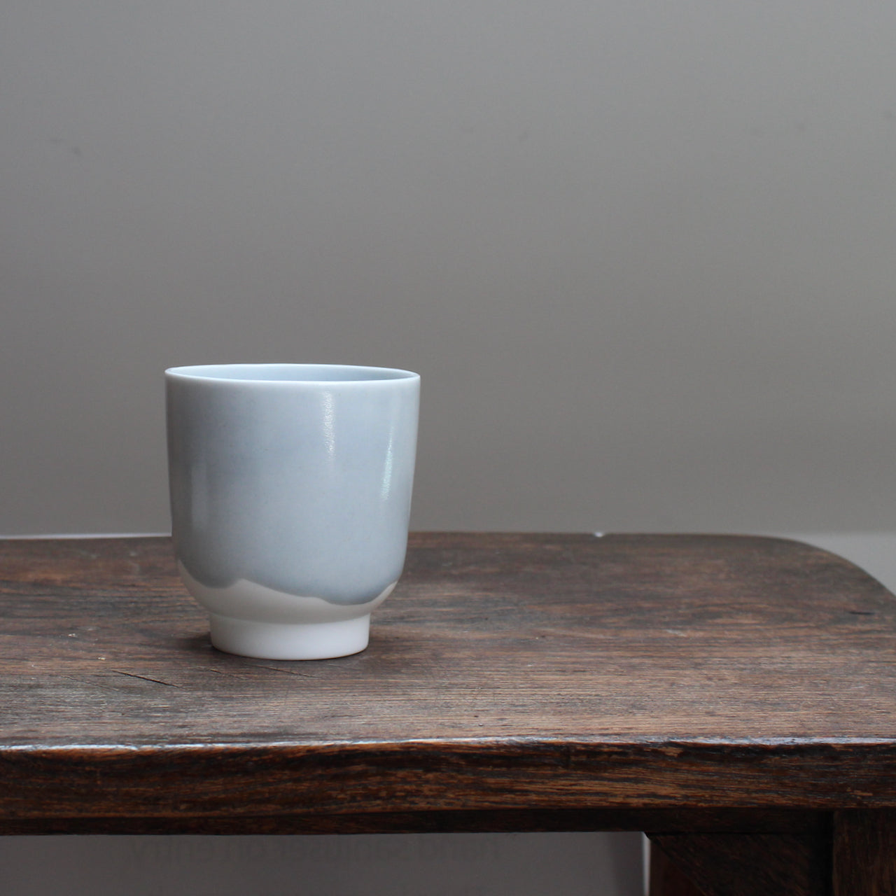 Small kiln shaped pale bluSmall pale ceramic beaker  with a white bottom on a wooden table