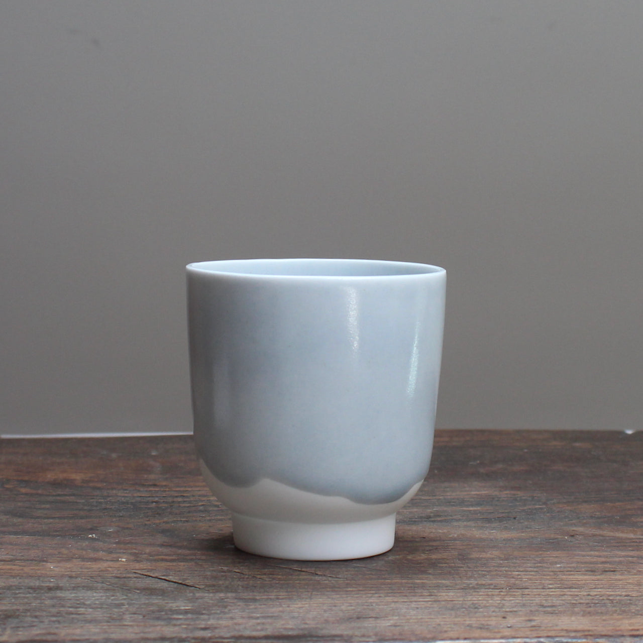 Small kiln shaped pale bluSmall pale ceramic beaker  with a white bottom on a wooden table