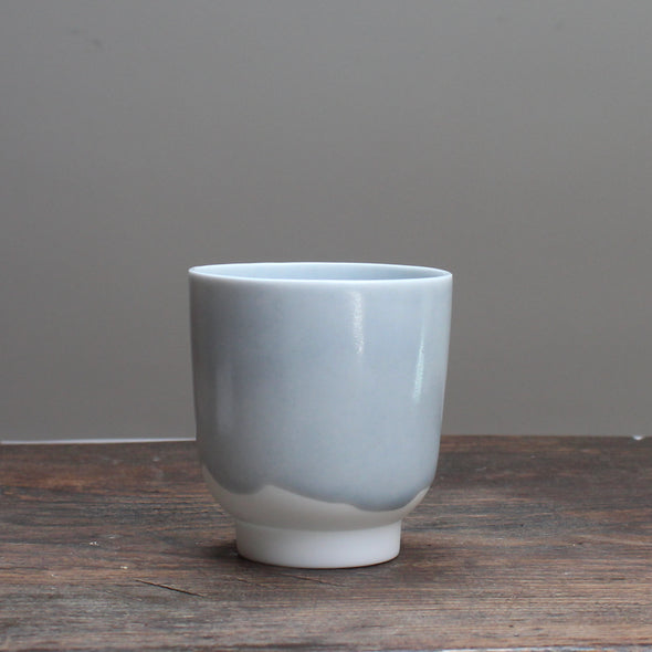 Small kiln shaped pale bluSmall pale ceramic beaker  with a white bottom on a wooden table 